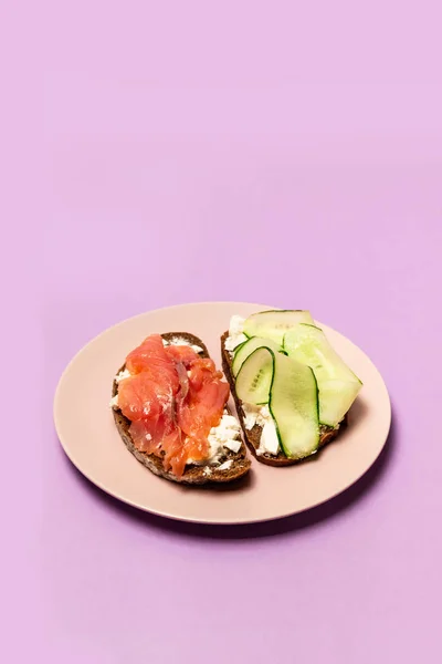 Sandwich con salmón, pepino, queso y pan de centeno de cerca sobre un fondo lila. Concepto de dieta y obesidad —  Fotos de Stock