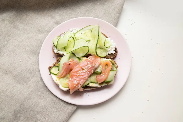 Sandwich frais savoureux avec du poisson rouge, du concombre de fromage feta et du pesto sur une assiette en céramique rose sur fond violet — Photo