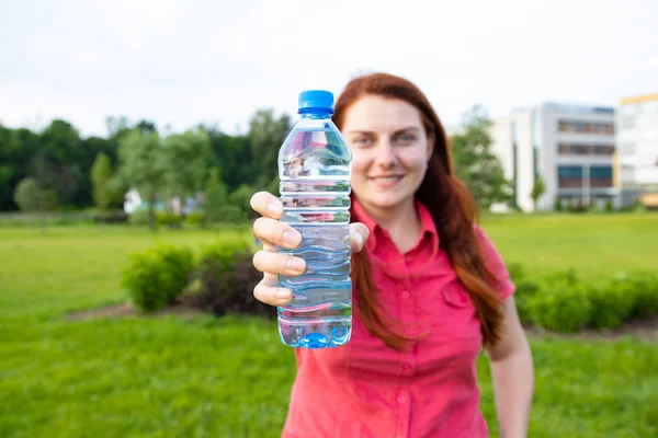 Young girl in bright summer clothes holds a plastic bottle of water on the background of the park