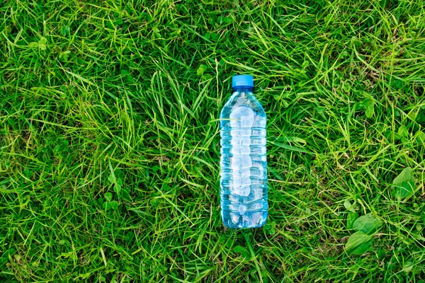Fles water op het groene gras. Gras en plastic gazon. Natuurlijk licht. Dik zacht gras. — Stockfoto