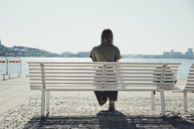 Kız nehir kıyısında bir bankta oturur ve güzel bir gün batımı sahiptir. Gölde altın gün batımı.