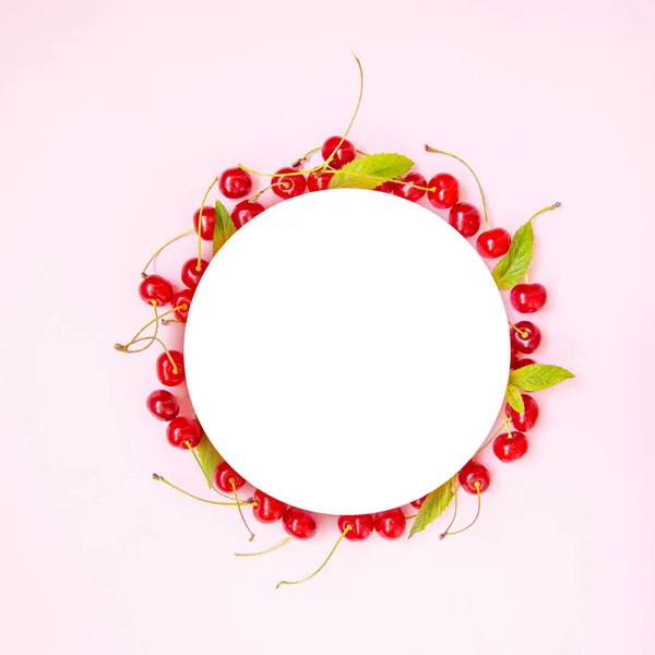 Food circle frame of red ripe cherries with green mint leaves on a pink background. View from above. Flat lay