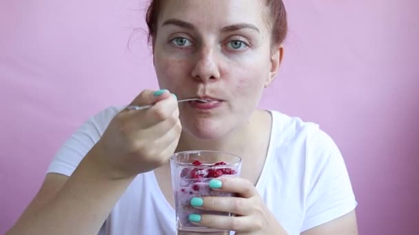 Young girl holds a glass with granola with natural yogurt, fresh raspberries, honey and eats her breakfast. — Stock Video