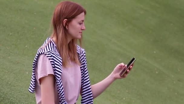 Jeune fille parlant sur un téléphone portable assis sur un banc dans un parc — Video