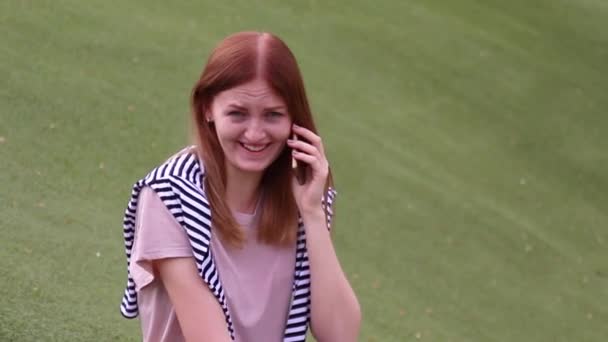 Chica joven hablando en el teléfono móvil sentado en un banco en un parque — Vídeos de Stock