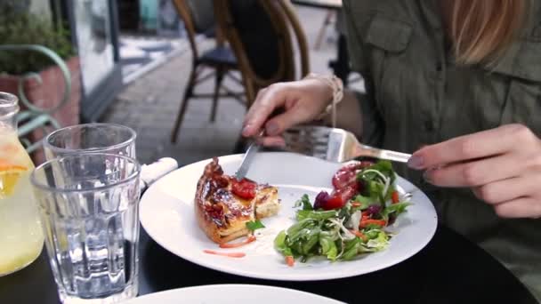 Vrouwelijke handen knippen een stukje pizza op een bord in een gezellig straat café. — Stockvideo