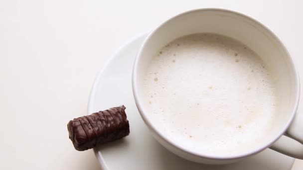 White ceramic cup with latte with a piece of chocolate candy on a white table — Stock Video