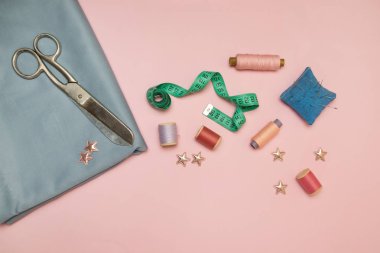 İğne işi aletleri, dikiş için örme iğne ucu, makas ve metin için kopya alanı ile pembe bir arka plan üzerinde iplik renkli makaralar