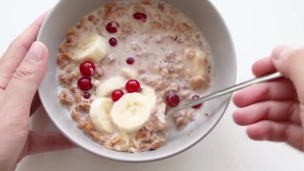 Female hand interferes with oatmeal with berries and a banana in a plate. Breakfast concept — Stock Video