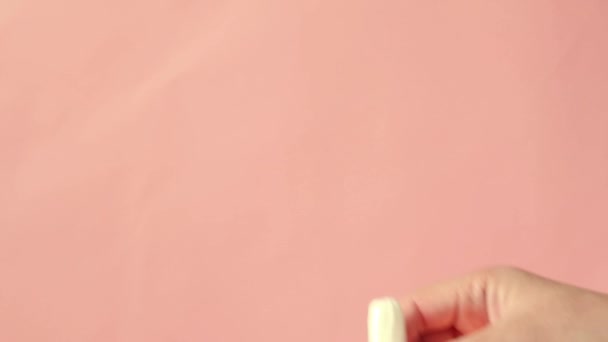 Female hand shows a tampon on a pink background. Women health concept, zero waste alternatives — Stock Video