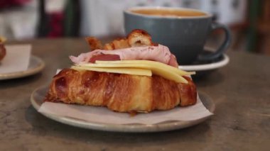 Bir kafede bir masada lat ile seramik tabak üzerinde peynir ve jambon ile taze pişmiş kruvasan.
