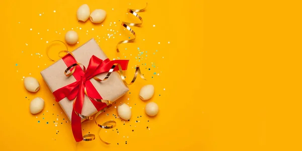 Fondo concepto Pascua de regalo o presente caja con cinta de atlas rojo y estrellas confeti sobre fondo amarillo.Decoraciones de vacaciones —  Fotos de Stock