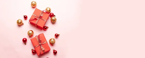 Karácsonyi ajándékdoboz szatén szalaggal, arany és piros golyókkal rózsaszín háttérrel. Karácsony, tél, újév koncepció. — Stock Fotó