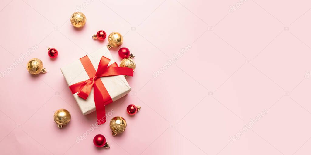Christmas gift box with satin red ribbon, gold and red balls on a pink background. Flat lay, top view, copy space