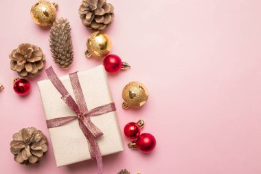 Kırmızı kurdeleli, çam kozalaklı, pembe arka planda altın ve kırmızı toplu hediye paketinin yaratıcı yeni yıl kompozisyonu.