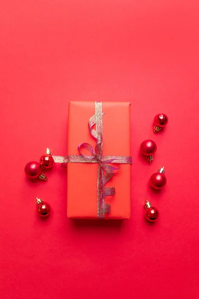 Creative Christmas composition with red present box, ribbons, red big and small balls, holiday decorations on red background. Flat lay, top view, copy space — ストック写真