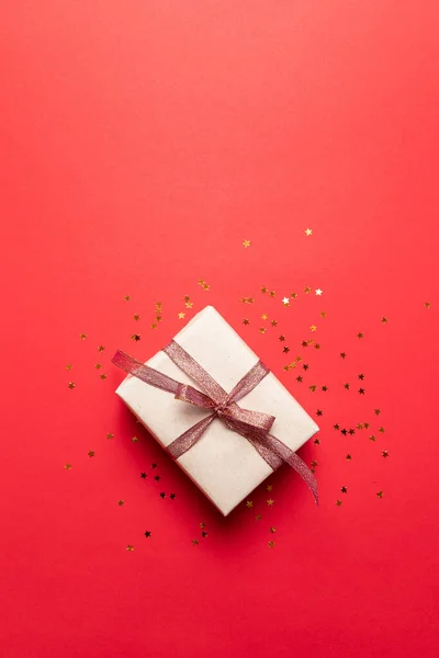 Vista superior de la caja de regalo con decoración de estrellas de oro sobre fondo rojo. Concepto mínimo para cumpleaños, día de la madre o boda . — Foto de Stock