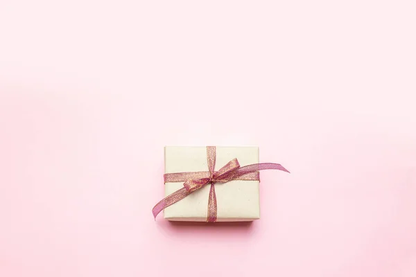 Mínimo concepto de Navidad caja de regalo artesanal sorpresa con lazo de cinta dorada sobre fondo rosa pastel . — Foto de Stock