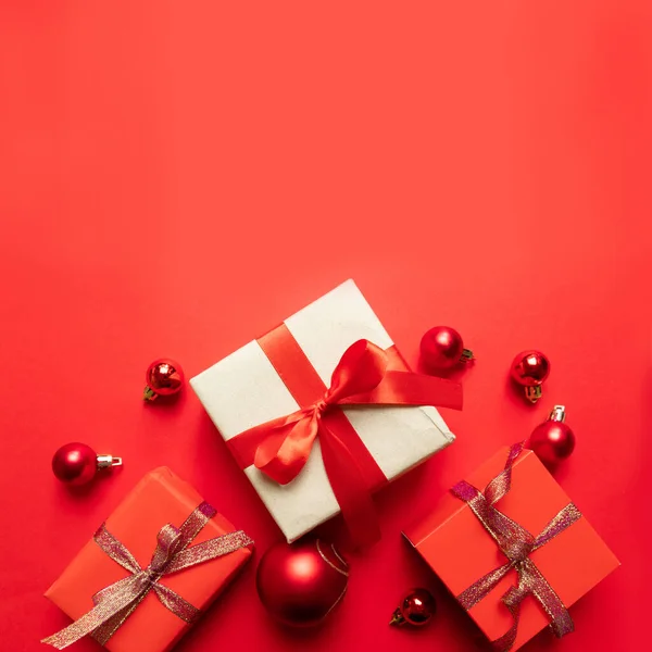 Creative Christmas composition with red present box, ribbons, red big and small balls, holiday decorations on red background. Flat lay, top view, copy space — ストック写真