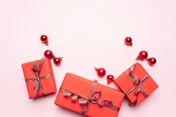 Cajas de regalo rojas navideñas, bolas sobre fondo rosa pastel. Tarjeta de felicitación de celebración festiva con espacio para copiar — Foto de Stock