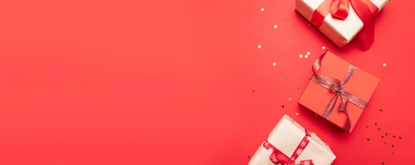 Kreatywna kompozycja z prezentami lub prezentuje pudełka ze złotymi kokardkami i konfetti gwiazdkowe na czerwonym tle. Płaska kompozycja świecka na urodziny, Boże Narodzenie lub ślub. — Zdjęcie stockowe