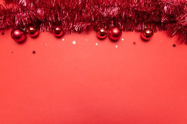 赤い背景にクリスマスティンセルとクリスマスの組成。クリスマス、冬、新年のコンセプト。フラットレイアウト、トップビュー、コピースペース. — ストック写真