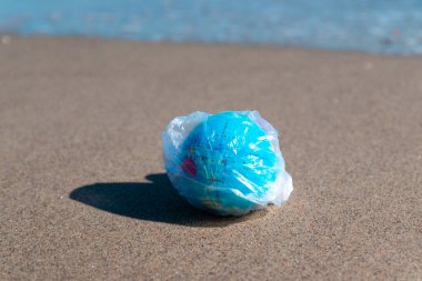 Çevre kirliliği kavramı. Plastik torba ve Dünya gezegeni güneşli bir günde okyanus kenarında.