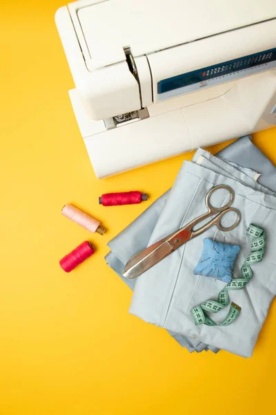 Vista superior de la máquina de coser con accesorios para coser, tijeras y una cinta métrica sobre un fondo amarillo con lugar para texto — Foto de Stock