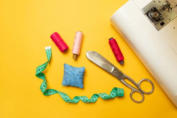 Composición moderna de la máquina de coser con accesorios para coser, tijeras y una cinta métrica sobre un fondo amarillo con lugar para texto — Foto de Stock