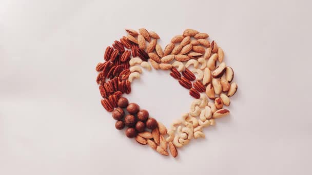 Bovenaanzicht van diverse smakelijke cashewnoten met hazelnoten en amandelen hartvormige noten op grijze achtergrond. Vrouwelijke hand zet noten, gezond voedsel — Stockvideo