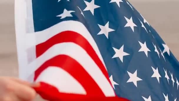 Close-up van mensenhanden houden Amerikaanse vlag op het strand in de buurt van zee golven. — Stockvideo