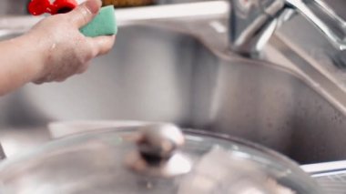 Kadın elleri bulaşık deterjanı sürerler, yavaş çekimde. Mutfak temizleme konsepti