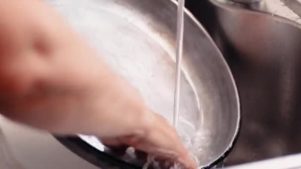 Weibliche Hände waschen die Pfanne mit Schwamm und Spülmittel unter fließendem Wasser in der Spüle — Stockvideo