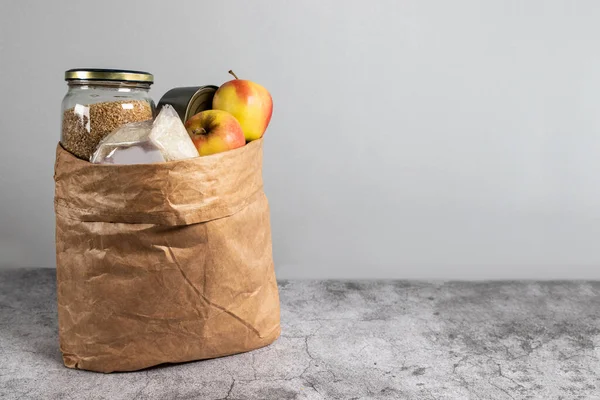 Donation paper bag food supplies for people in isolation on gray background with copy space.
