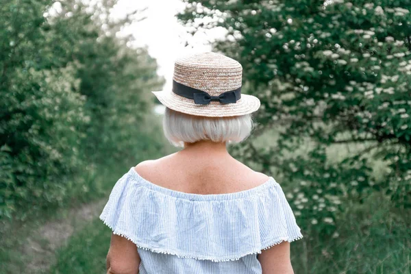 Back view of a blonde girl in straw hat with a bow in the summer garden. Lifestyle and summer concept.