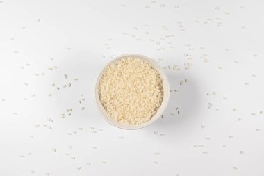 Beyaz zemin üzerinde yeşil tabakta organik çiğ pirinç taneleri.