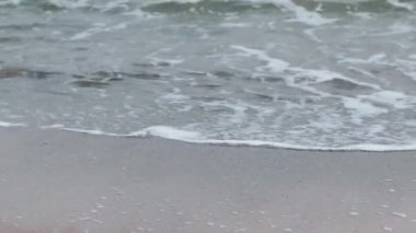 Deniz dalgaları bulutlu bir günde kumlu kıyıya vurur. Seyahat ve tatil kavramı.