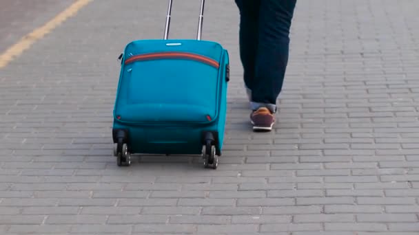 バックパックとブルーのキャリーオンスーツケースを持つブロンドの女性が電車、リアビューにプラットフォームに沿って歩く — ストック動画