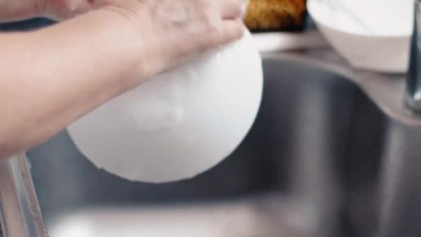 Κοντινό πλάνο γυναικείων χεριών που πλένουν βρώμικα πιάτα με απορρυπαντικό και σφουγγάρι στον νεροχύτη της κουζίνας — Αρχείο Βίντεο