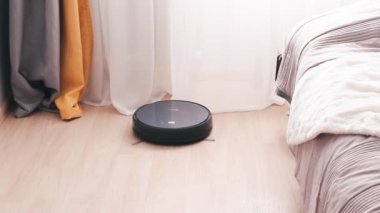 Siyah robot elektrikli süpürge güneşli bir günde oturma odasının kirli zeminini otomatik olarak temizler..