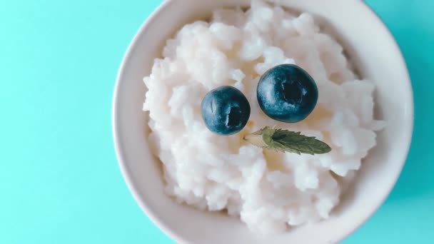 Platt låg rismjölk gröt med blåbär och mynta på en blå bakgrund. Smaklig hälsosam frukost — Stockvideo