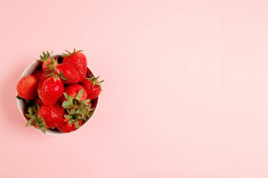 Pembe arka planda taze çilekli kahvaltı kasesi. Yaz kompozisyonu, dikey fotoğraf