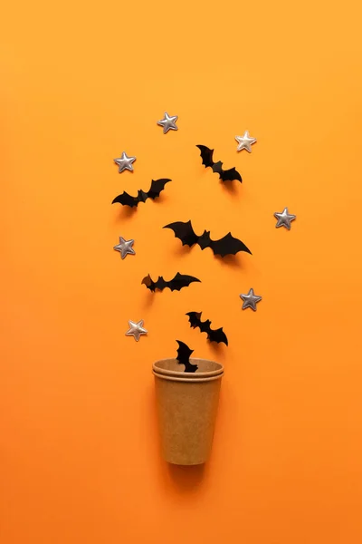 Halloween concepto de vacaciones de murciélagos negros vuelan fuera de la taza de papel sobre un fondo naranja . —  Fotos de Stock