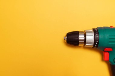 Sondajlı bir kablosuz matkap, ayrıca sarı arka planda tornavida olarak çalışıyor. Mininmalistik düzlük.