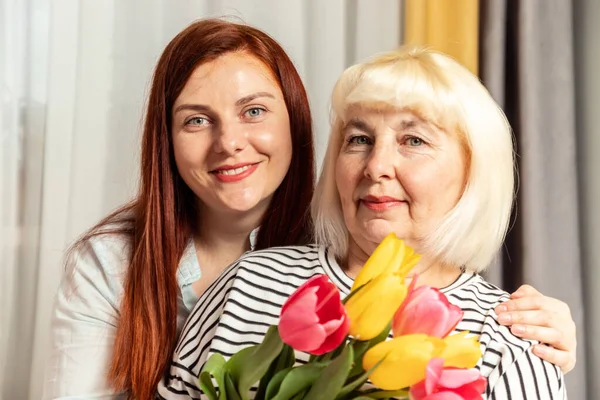 Hermosas mujeres jóvenes y adultas alegres con un ramo de flores de tulipanes con copyspace en casa. Día Internacional de la Mujer. —  Fotos de Stock