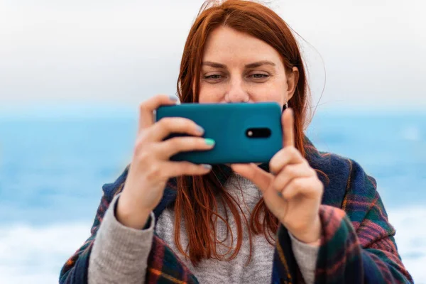 Turystyczny biały rude włosy kobieta uśmiecha się, robi zdjęcia lub nagrywa wideo na telefon na plaży w pobliżu oceanu, koncepcji wakacje — Zdjęcie stockowe