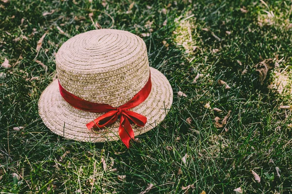 Beautiful straw summer hat with red ribbon on green grass