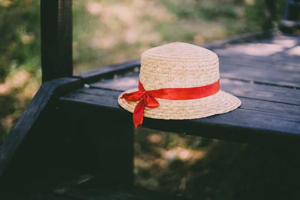 Summer straw hat with red ribbon lies on black wooden step in the park