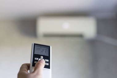 Uzaktan kumandayı tutarken yakın çekim. Evdeki odada uzaktan kumandalı klima ayarları..