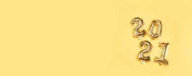 2021 altın folyo balonu sarı arka planda havada uçuyor. Yılbaşı ve yeni yıl dekorasyon elementi pankartı için kavram tasarımı